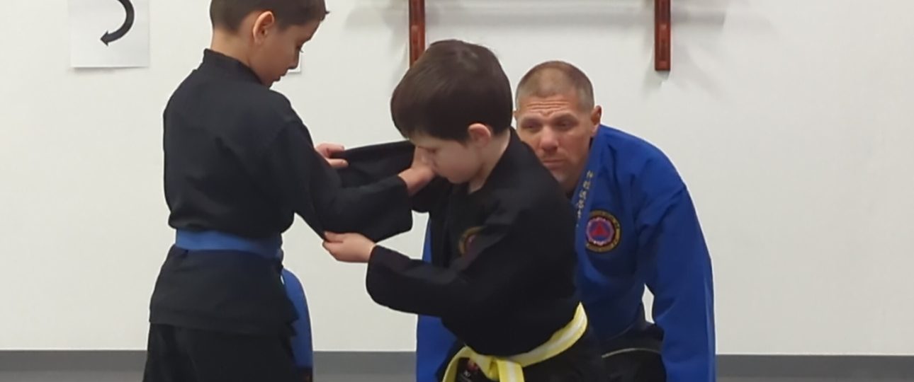 two kids grappling in a martial art class with the instructor watching at Shin Gan Dojo