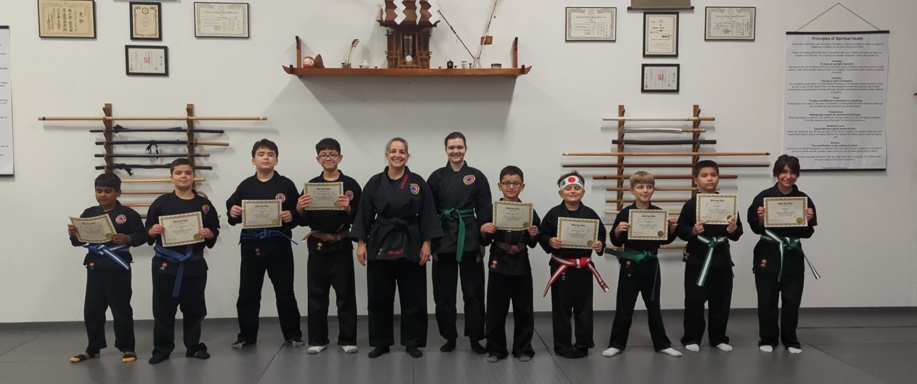 UDA20260822_105645 - Martial Arts Dojo in Liberty Hill, Texas Martial arts kids in black uniforms holding certificates for belt rank promotions with Instructor and Assistant Instructor at Shin Gan Dojo in Liberty Hill Texas