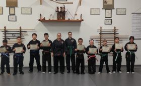 Martial arts kids in black uniforms holding certificates for belt rank promotions with Instructor and Assistant Instructor at Shin Gan Dojo in Liberty Hill Texas