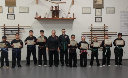 Martial arts kids in black uniforms holding certificates for belt rank promotions with Instructor and Assistant Instructor at Shin Gan Dojo in Liberty Hill Texas